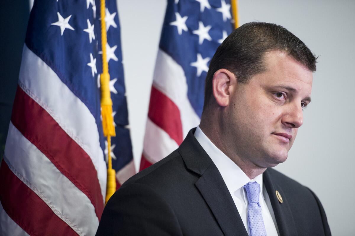 A closeup of David Valadao with two American flags in the background.