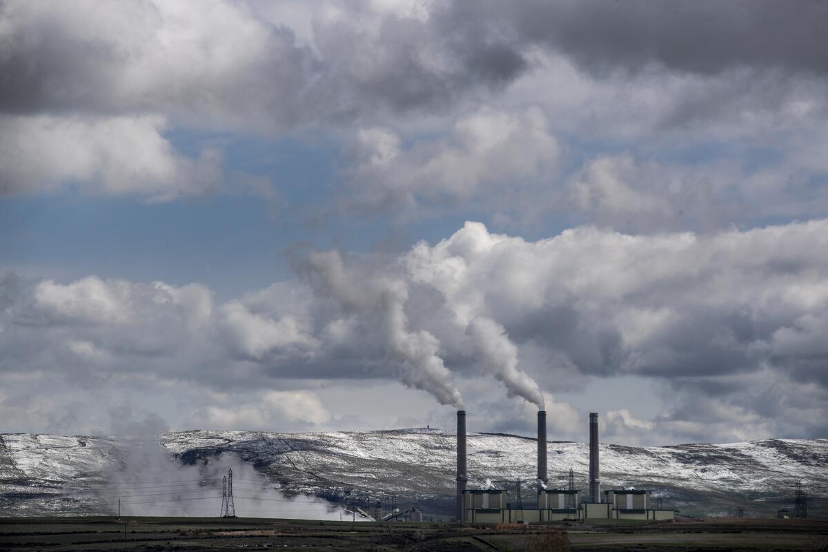 A power plant with snow-capped hills behind it. 