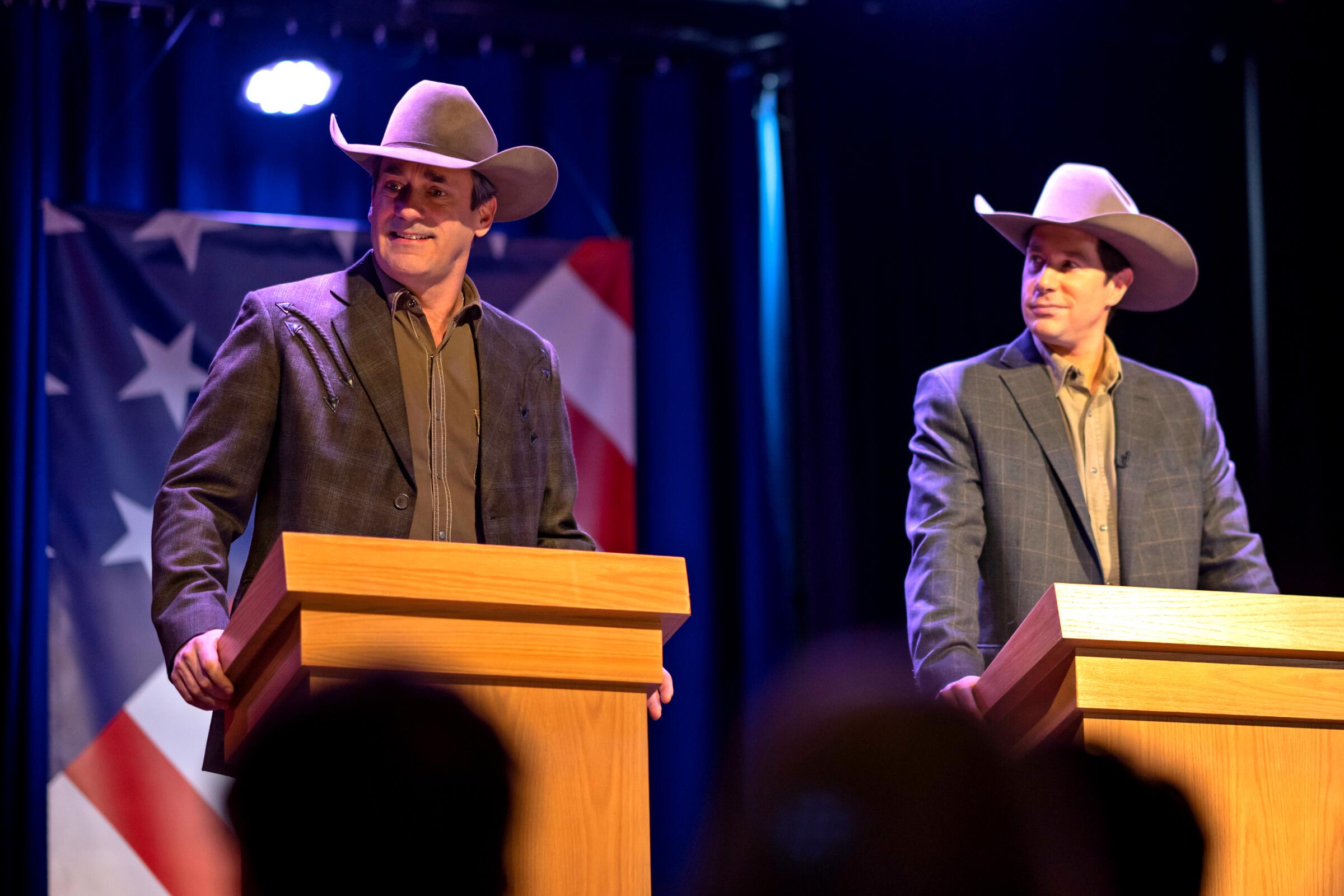 Two men, dressed alike in cowboy hats, stand at podiums in a scene from "Fargo" Season 5.