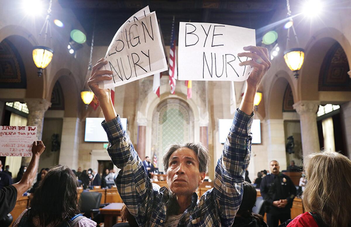 A man holds up two signs that say "resign Nury" and "bye Nury"