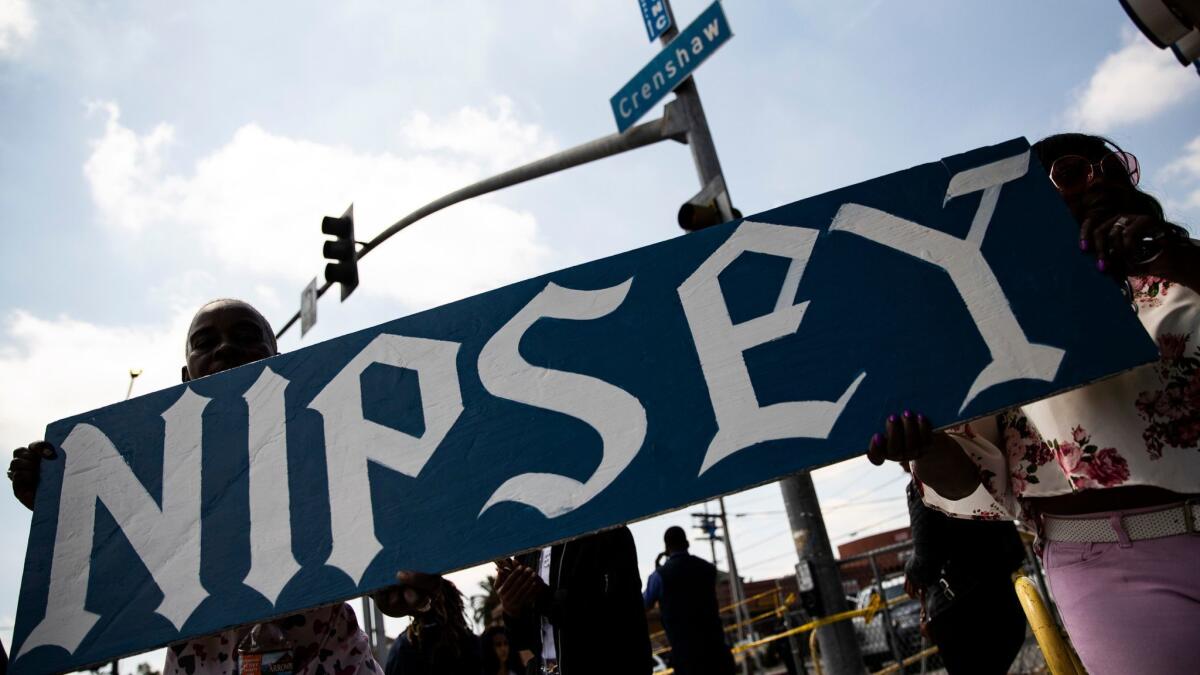 Two women hold a banner reading "Nipsey" at the Slauson Avenue and Crenshaw Boulevard intersection.