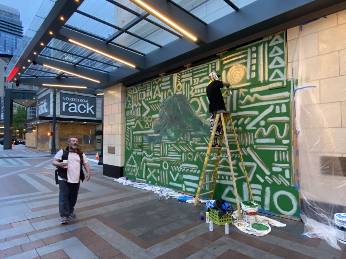 Procter nears completion of a mural on Nordstrom in downtown Seattle as a man walks by.