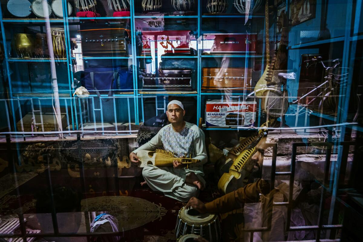 A man in a blue tunic practices rubab seen through a window