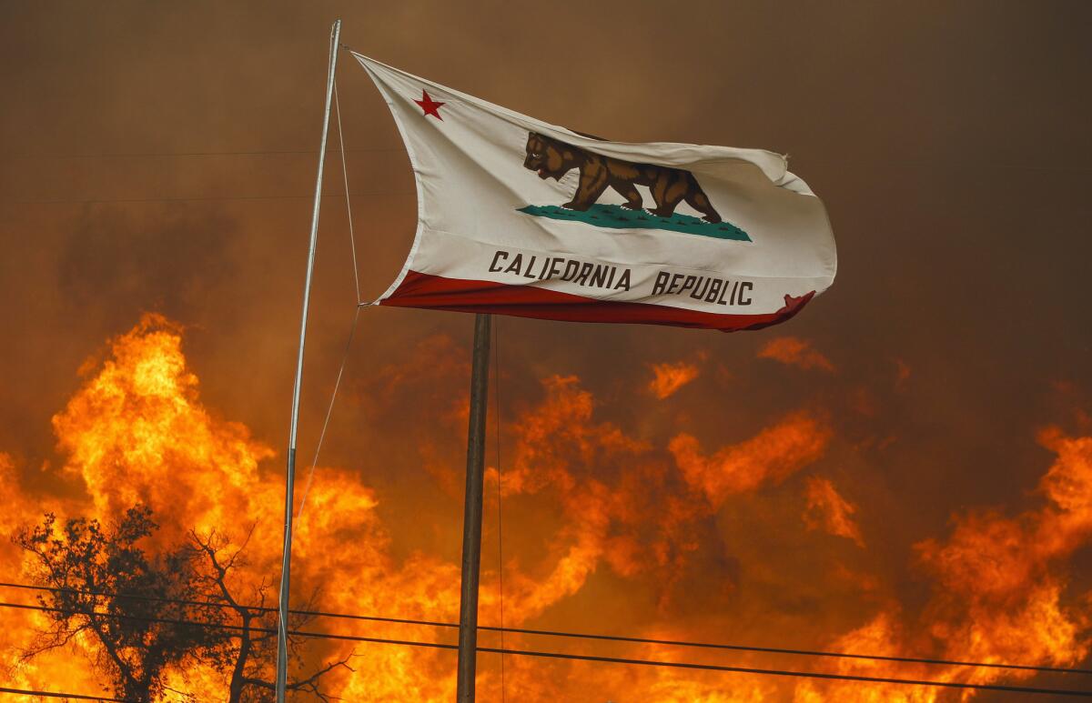 The California state flag flies next to a home on Highway 94 south of Potrero as huge flames roar behind it. San Diego Gas & Electric is asking the California Public Utilities Commission for an increase in shareholder returns, citing wildfire risks in the state.