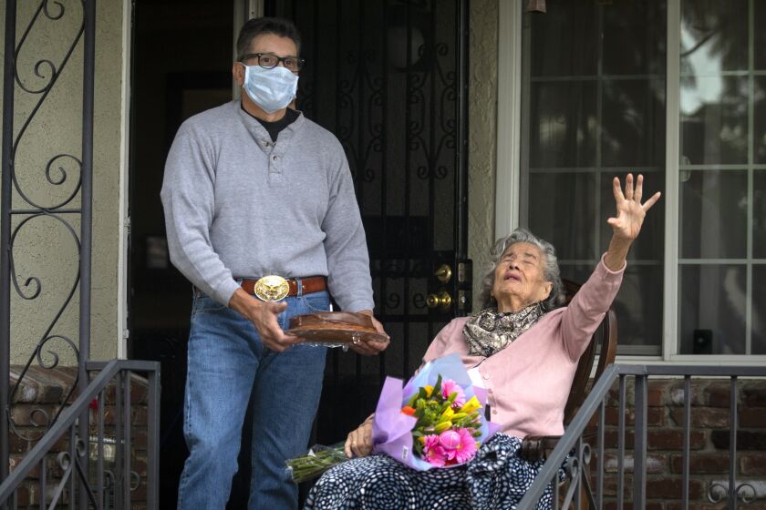 ALHAMBRA, CA - APRIL 06: During the coronavirus pandemic Socorro Majarro Duran, right, celebrates her 91st birthday on Monday, April 6, 2020 in Alhambra, CA. Her son Guillermo Mojarro holds her birthday cake while Socorro's family drives past in a carivan in celebration. Her family sang to her from a distance and wished her a happy birthday. The family celebrated three birthdays today as the carivaned from house to house. (Francine Orr / Los Angeles Times)