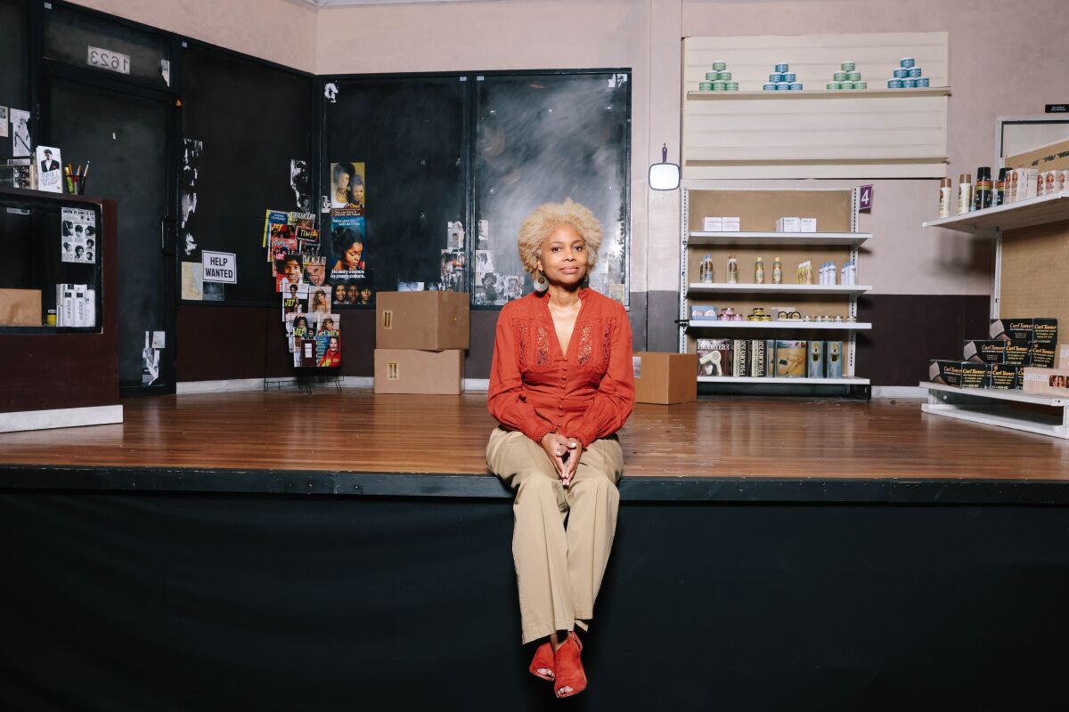 A woman in a dark orange top and beige pants sits on a stage.