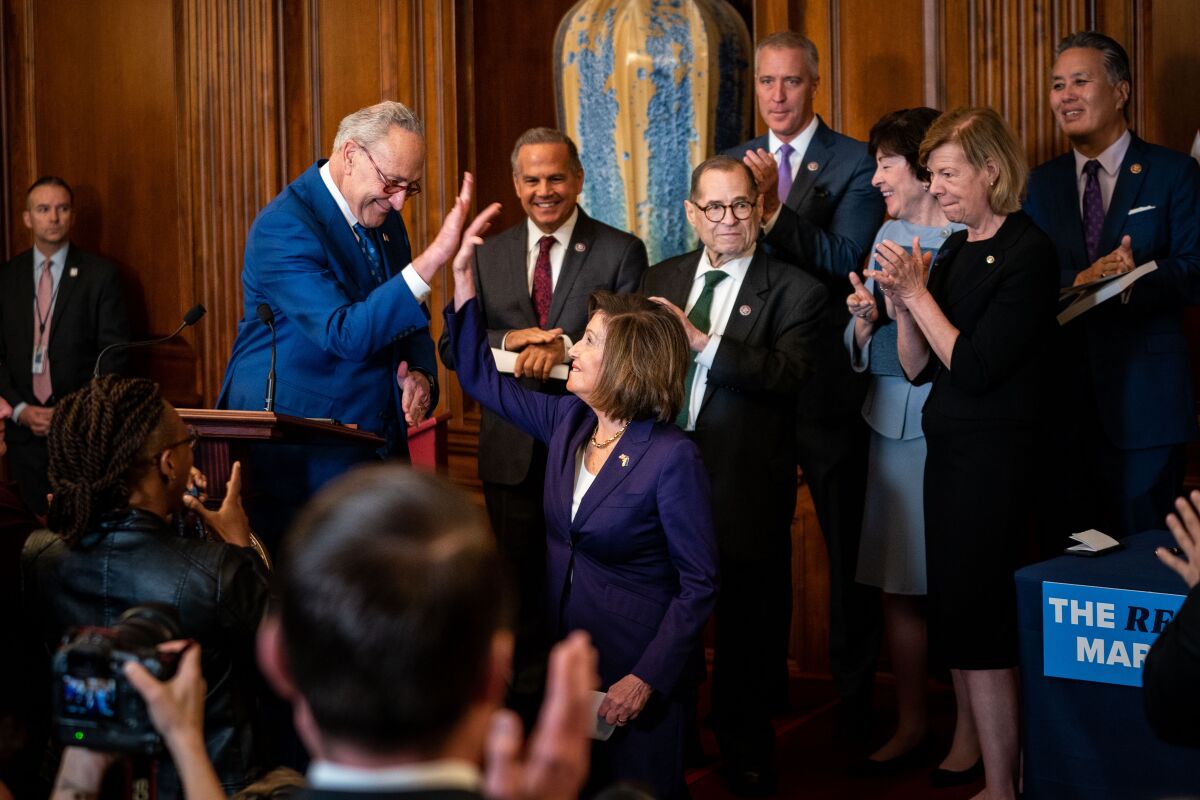 House Speaker Nancy Pelosi and Senate Majority Leader Charles E. Schumer high-five each other as other lawmakers stand by.
