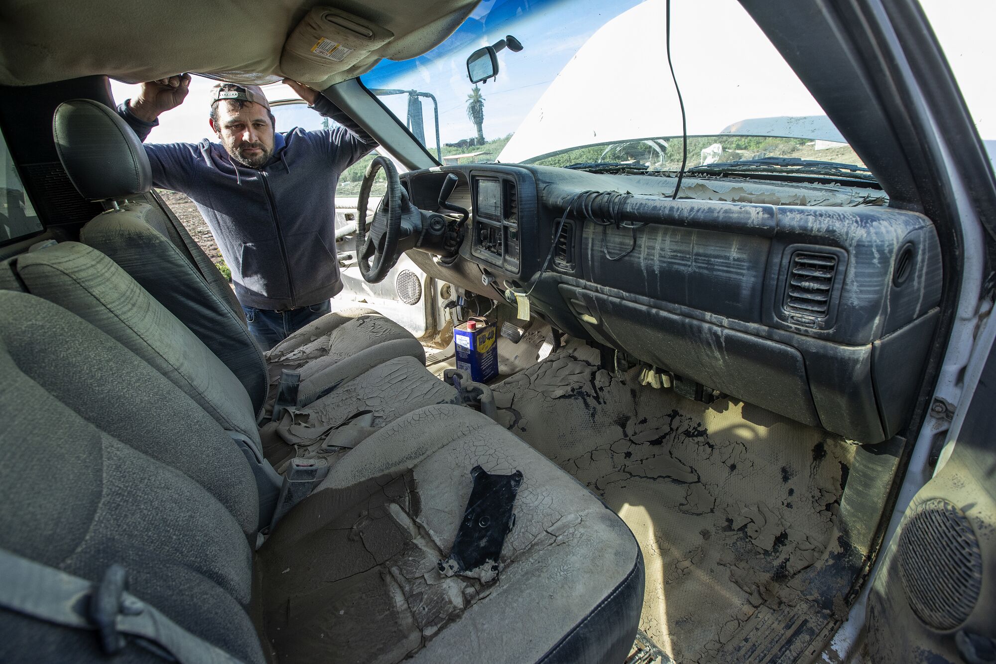 A man peers at the mud-caked interior of a truck.