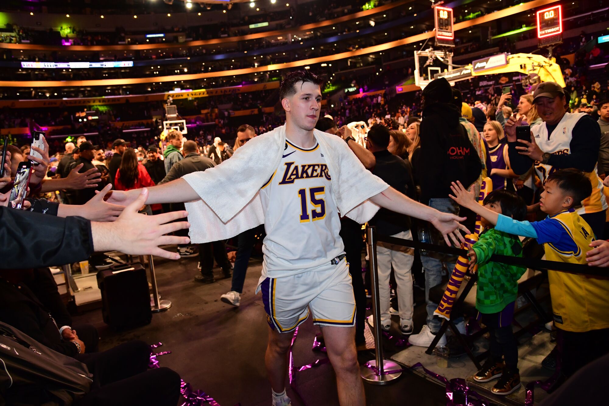 Lakers guard Austin Reaves touches hands with fans as he walks off the court with a towel draped on his shoulders.