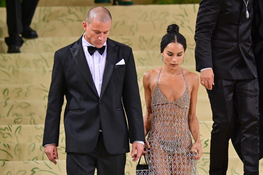 Channing Tatum in a tuxedo walking down golden stairs next to Zoê Kravitz in a sheer net gown. 