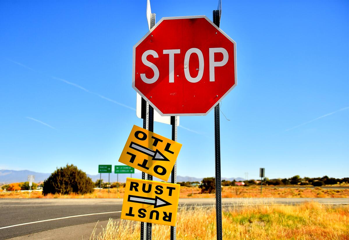 Signs with arrows attached to a stop sign direct people working on "Rust" toward the film's set in New Mexico.