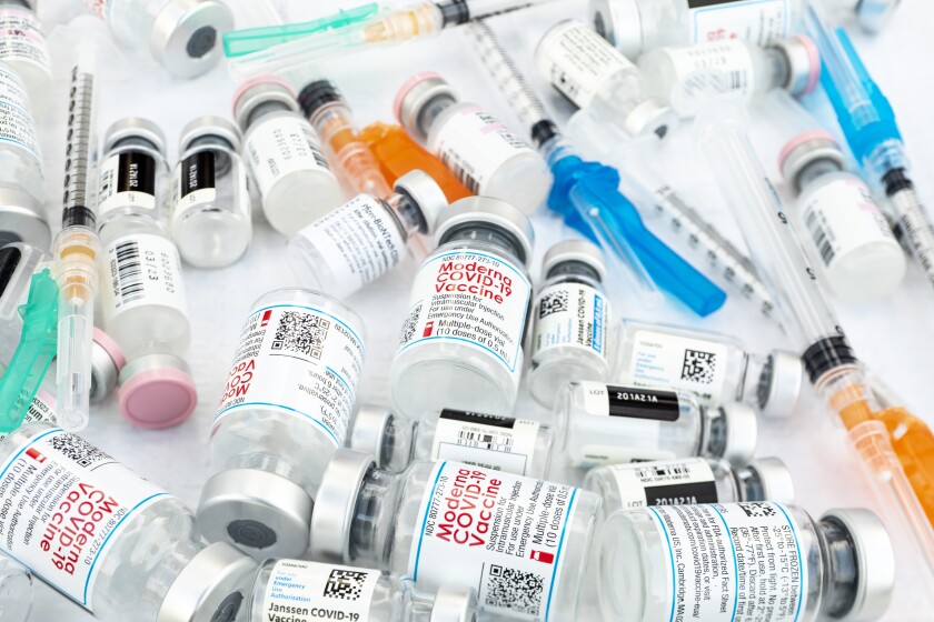 Bottles of COVID-19 vaccines lay alongside hypodermic needles 