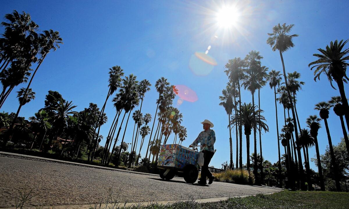 An ice cream vendor pushes a cart on the sidewalk that rings Echo Park Lake. City officials are urging lawmakers to approve new restrictions barring vending in public parks unless sellers have a license or permit to do so.