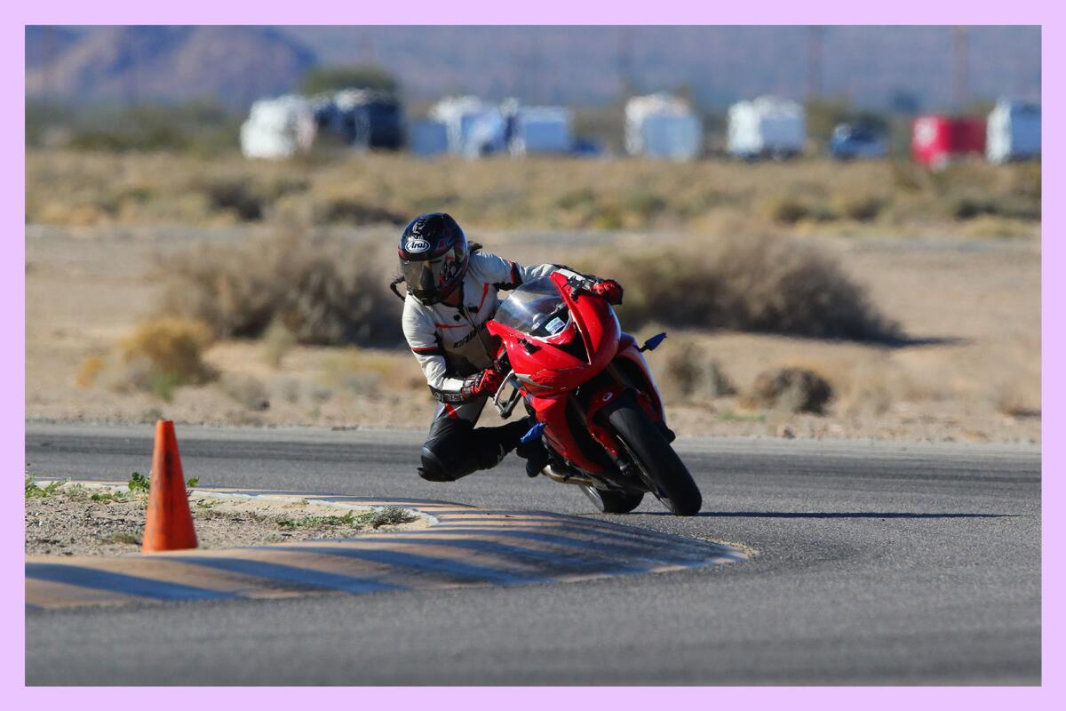 A helmeted person on a motorcycle leans into a curve next to an orange road cone