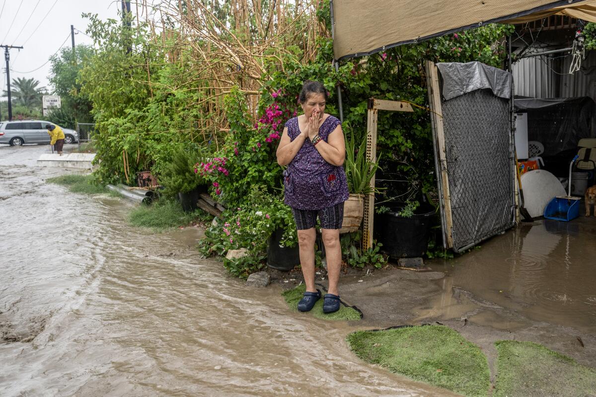 A woman watches as rain pushes flood waters into her driveway.