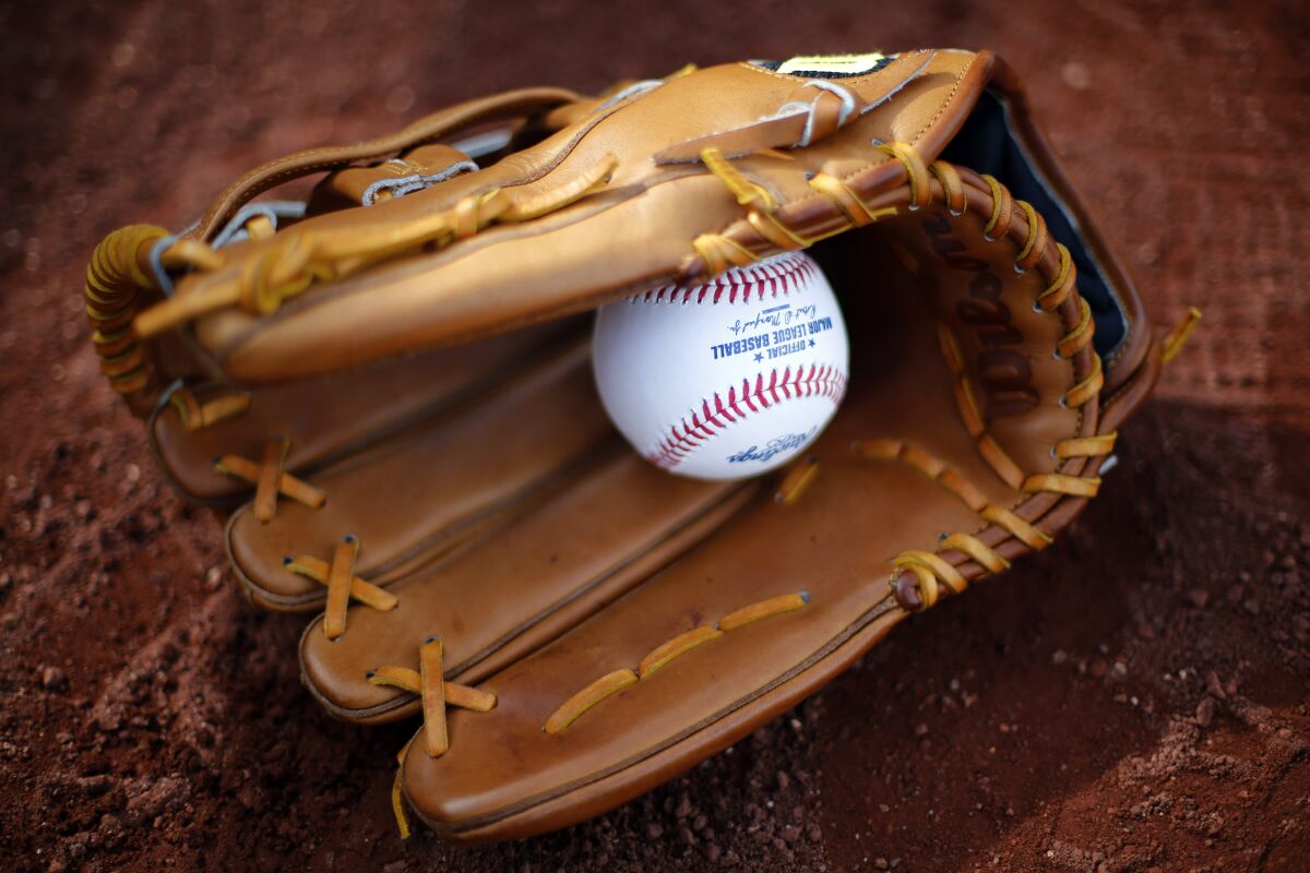 A baseball glove lies on the dirt with a baseball in it.