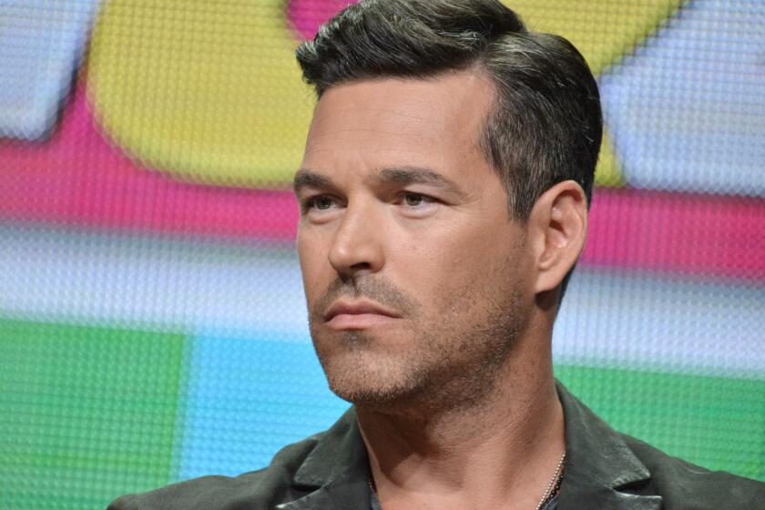 A man with short brown hair and stubble wearing a green collared shirt