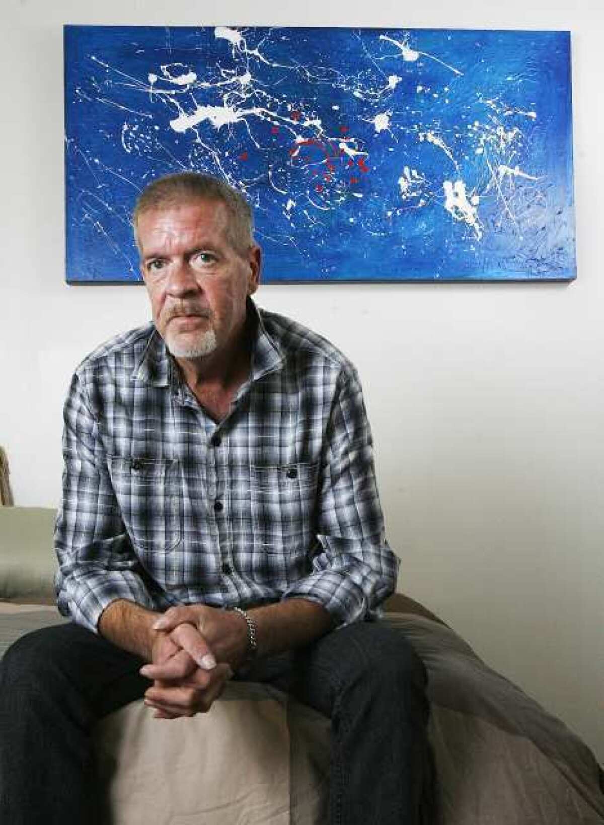 Lanny Allen sits on his bed with donated artwork behind him in his home in Glendale where he has lived for four weeks. Allen, with help from Ascencia, a nonprofit homeless services provider, and federal grants since he is a veteran, received the apartment and the furnishings through donations. He is happy and proud of his new life.