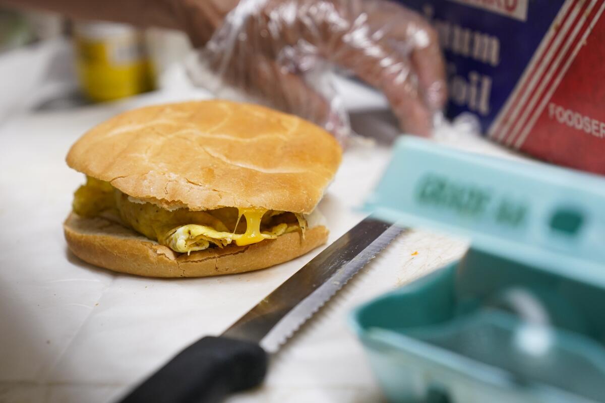 Héctor Pérez se prepara para envolver un sándwich de jamón, tocino y queso en una bodega del Bronx