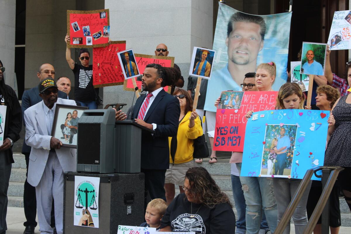 Adam Foss of Prosecutor Impact speaks as family members of those sentenced under the felony murder rule hold images of loved ones.
