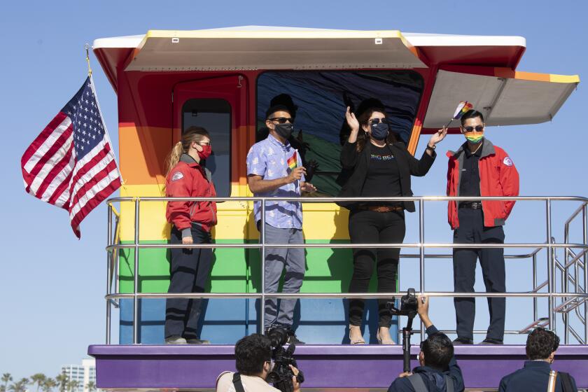 LONG BEACH, CA - JUNE 10: Long Beach Mayor Robert Garcia and Councilwoman Cindy Allen, flanked by lifeguards Devon Bebee, left, and Jeremy Rocha, celebrate the unveiling of a new rainbow-colored lifeguard tower at Long Beach to replace the one that burned down in March. The tower serves as a symbol of LGBTQ+ pride. Photographed on Thursday, June 10, 2021 in Long Beach, CA. (Myung J. Chun / Los Angeles Times)