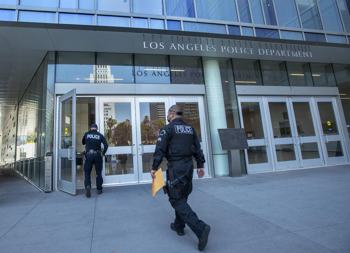 Two people in dark uniforms head for the doors of a building with the words Los Angeles Police Department 