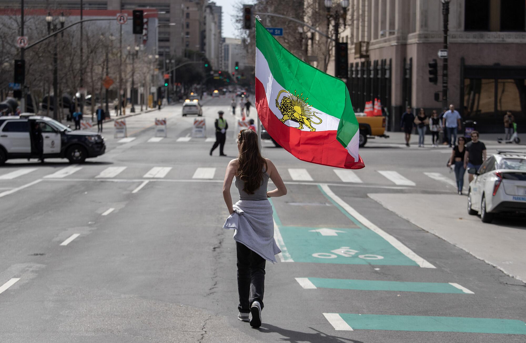 A woman carrying Iran's historical flag walks down the middle of a city street