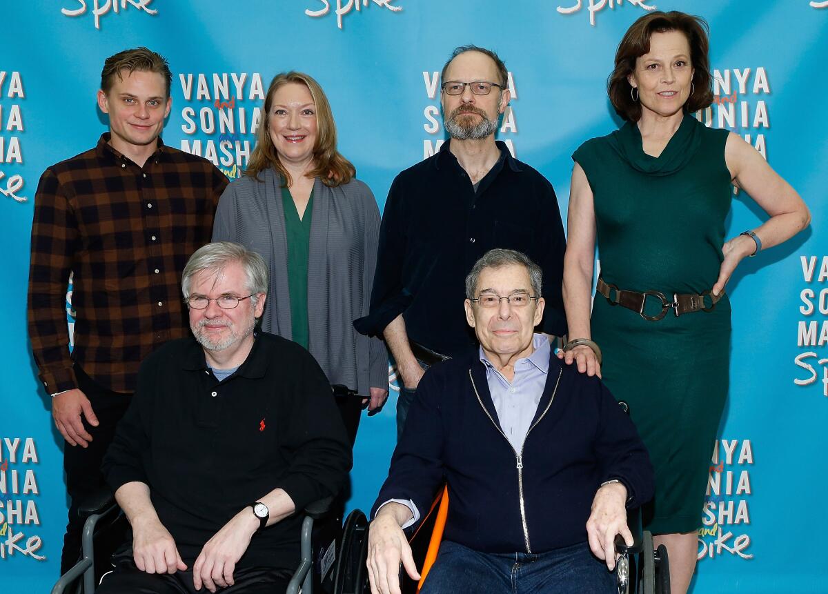 Four actors stand beside a seated playwright and director.