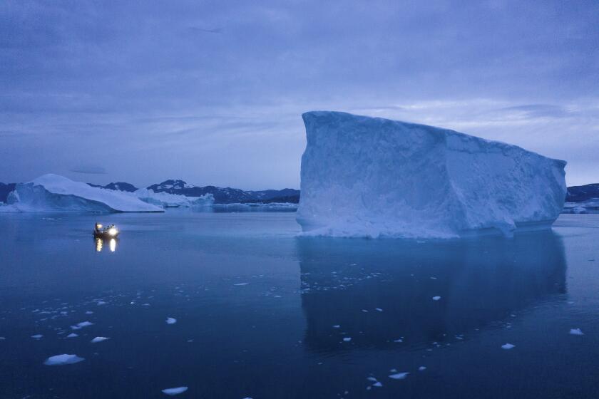 A boat navigates at night next to large icebergs in eastern Greenland. Greenland's ice has been melting for more than 20 years.