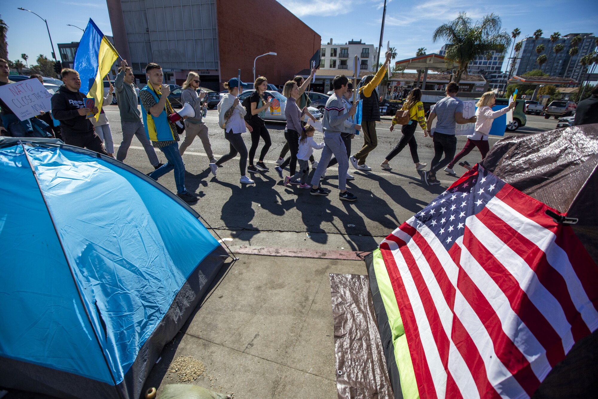 Demonstrators walk past a homeless encampment as they demonstrate their opposition to the Russian invasion of Ukraine.