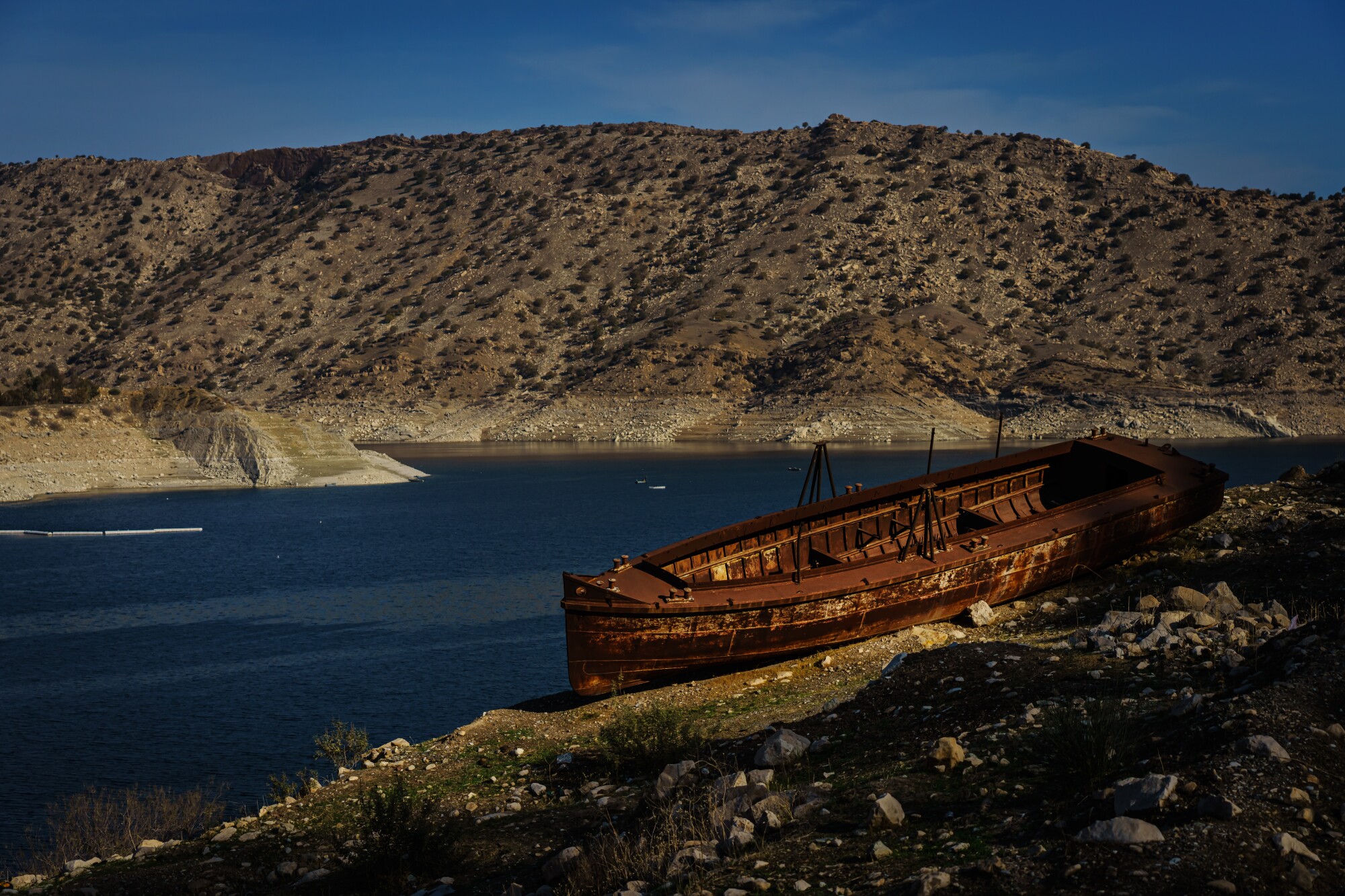 A view of water against a backdrop of mountains and a rusting boat in the foreground on the right. 