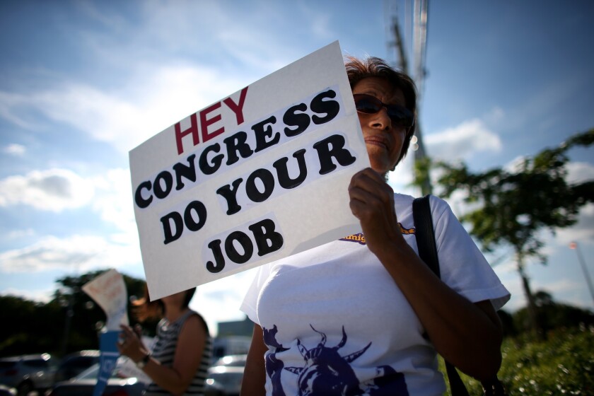 Omayra Hernadez holds a sign reading, "Hey Congress Do Your Job" as she and others gather in front of the Florida office of Rep. Mario Diaz-Balart (R-Fla.) to protest against the partial government shutdown.
