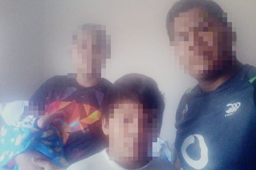 A mother holding a newborn baby with the father and brother standing nearby. Their faces are blurred.