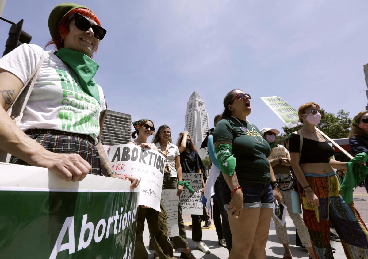 A group of women dressed in green stand outside and shout as they carry signs