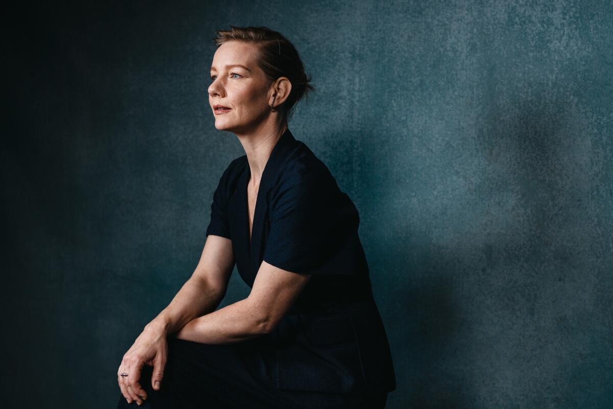 Sandra Hüller sits against a blue wall looking to the side for a portrait.