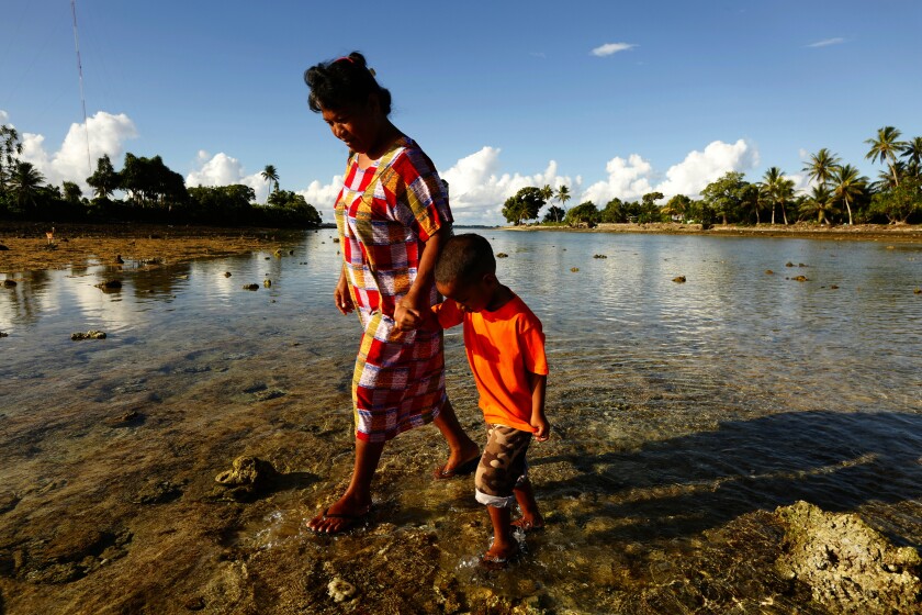 Josephine Noka walks with her son Jules during low tide in  the Marshall Islands.