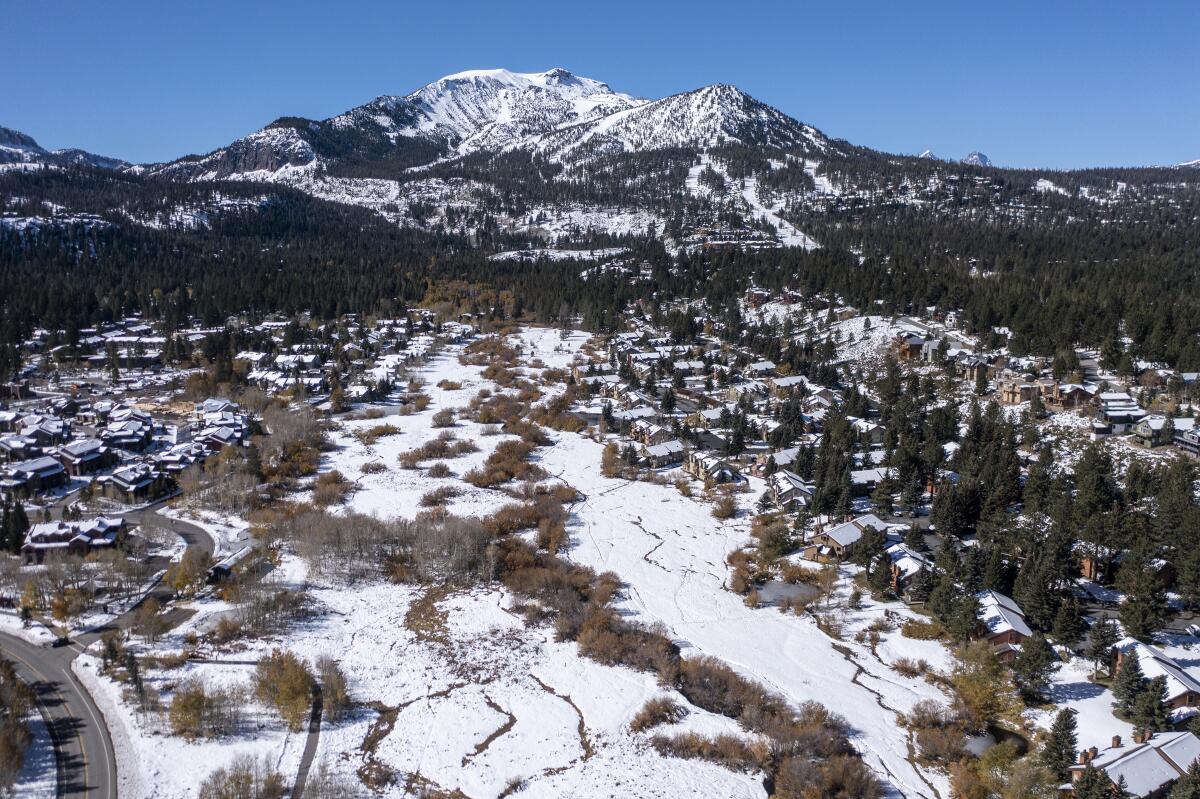 An aerial view of a neighborhood, open land covered with light snow and a mountain in the background.