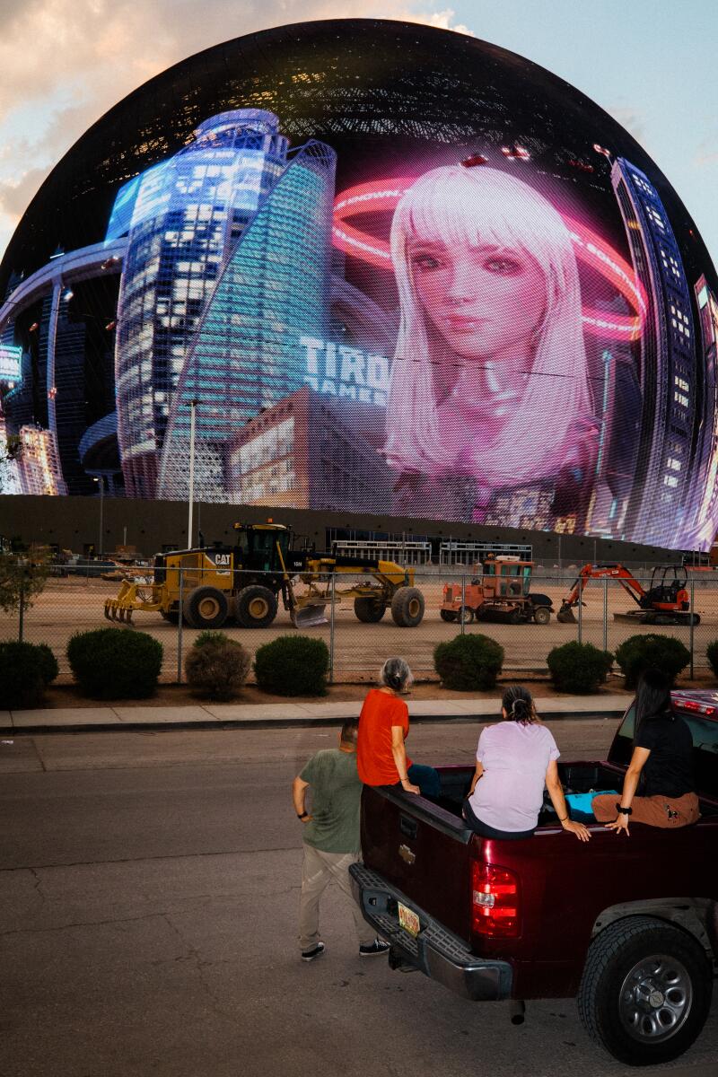 A man on a mobility scooter films Sphere with a moon overhead.