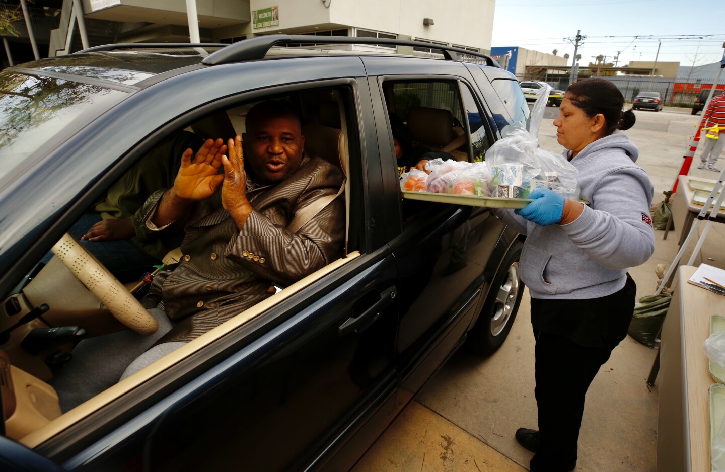 LOS ANGELES CA MARCH 18, 2020 -- Alake Ilegbameh said OMay God continue to bless youO over and over again as heOs driving his 3 school age children while he picks up food kits from LAUSD employee Benjula Prasad, right, being distributed to drivers in vehicles at Dorsey High School 3537 Farmdale Ave in Los Angeles Wednesday morning (Al Seib / Los Angeles Times)