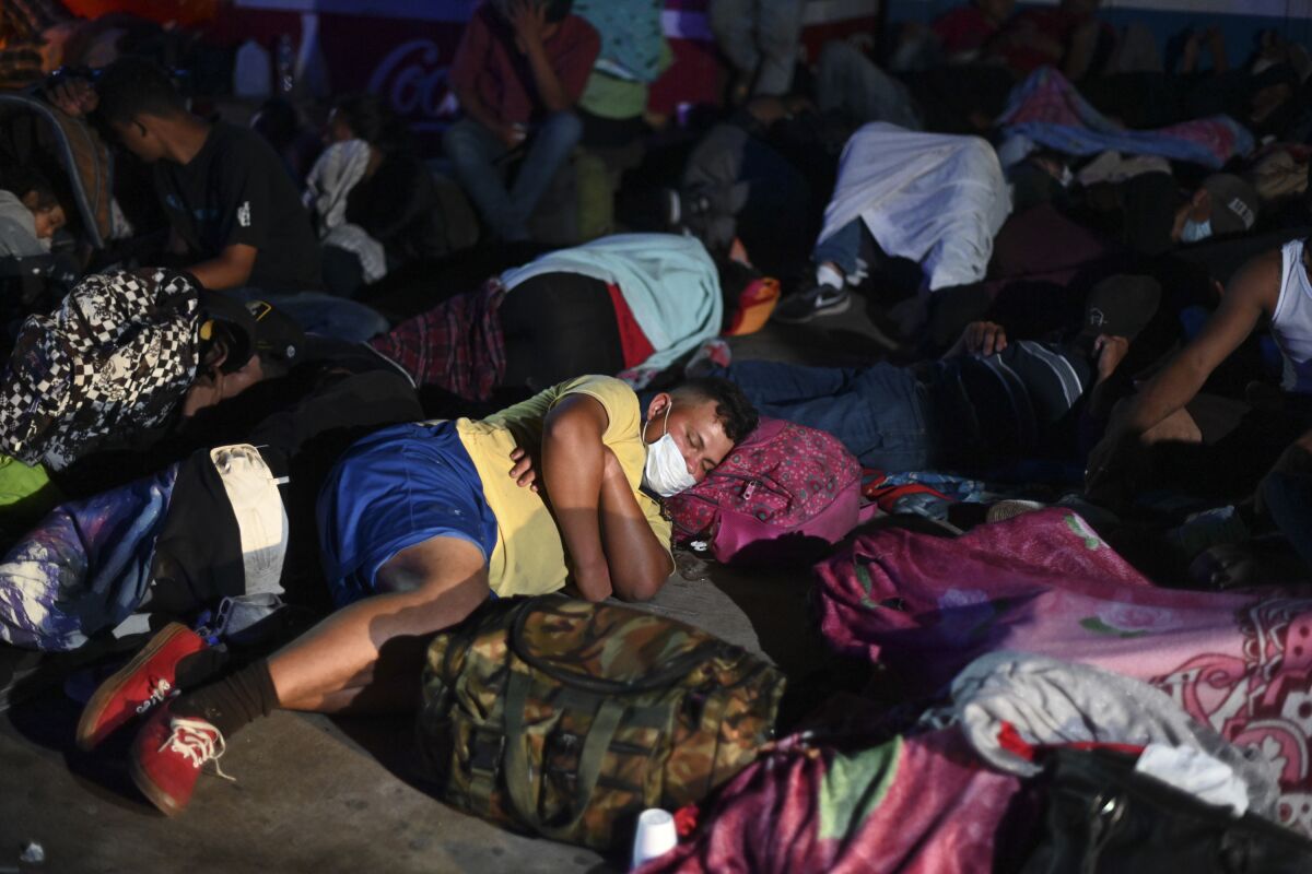 A man rests his head on a backpack to sleep among a crowd of migrants