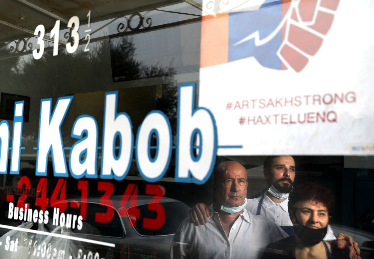 Three people reflected in window of restaurant with an Artsakh Strong sign