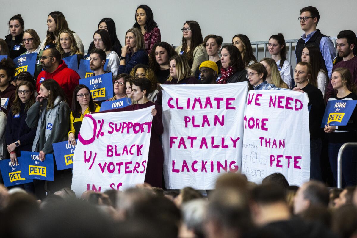 Protesters hold up signs as Democratic presidential candidate Pete Buttigieg, mayor of South Bend, Ind., starts to speak during a town hall in Coralville, Iowa.