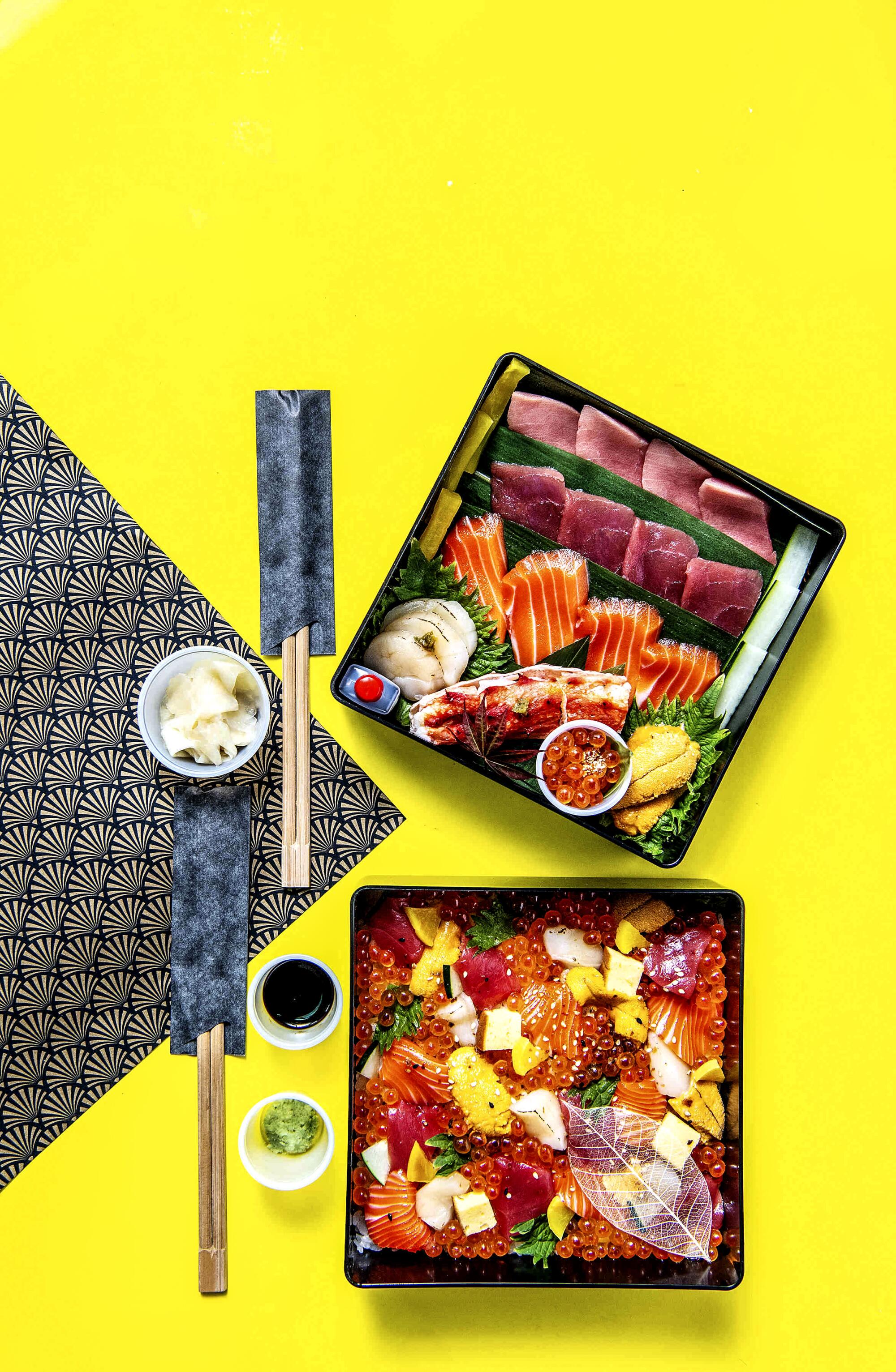 Two layers of a bento box filled with food with chopsticks nearby