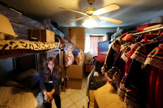 A woman seated on the lower half of a bunk bed in a room with a ceiling fan and clothes hanging on the right