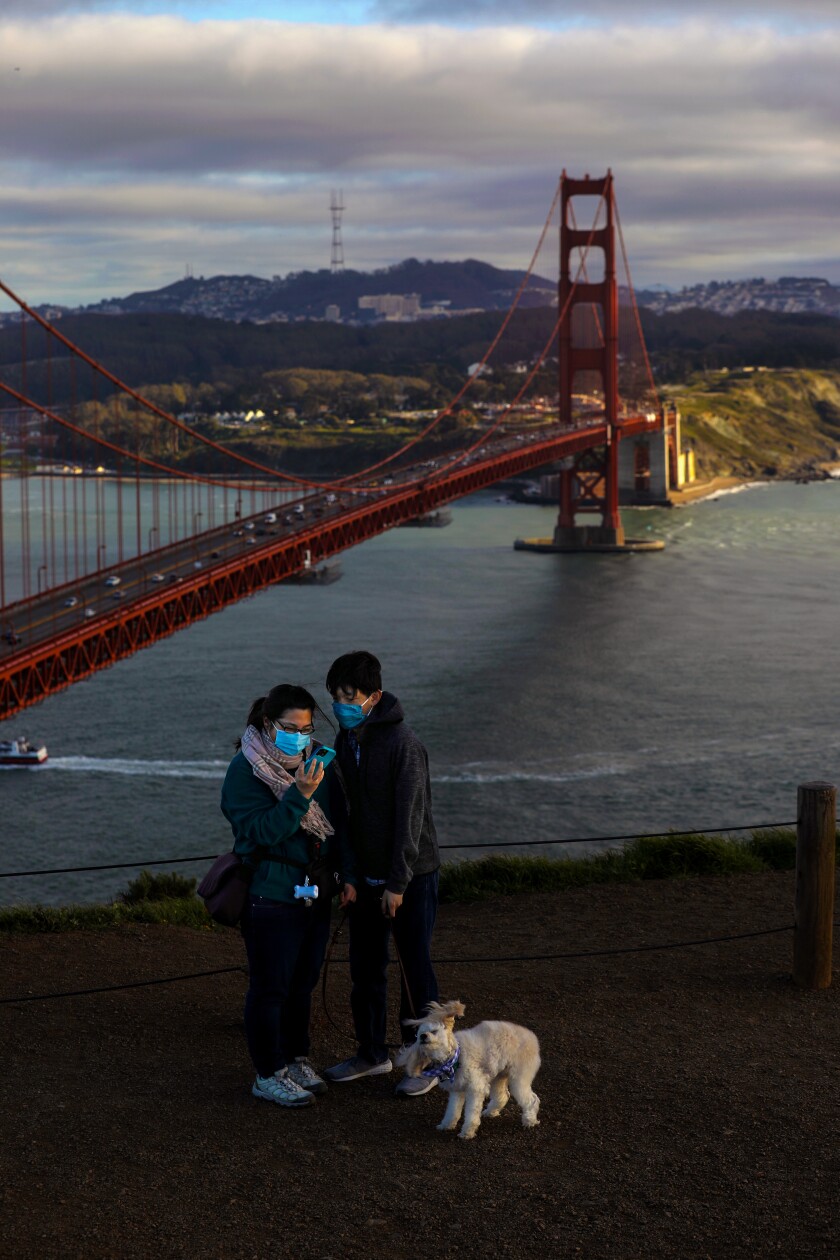 A couple with a dog take a selfie overlooking the Golden Gate Bridge.