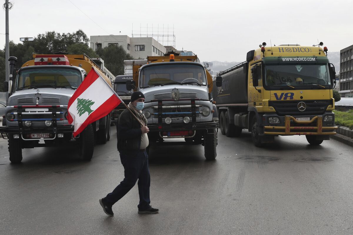 A truck driver holds a Lebanese flag as others drivers block a main highway with their vehicles during a general strike by public transport and workers unions paralyzed Lebanon in protest to the country's deteriorating economic and financial conditions, in Beirut, Lebanon, Thursday, Jan. 13, 2022. (AP Photo/Bilal Hussein)