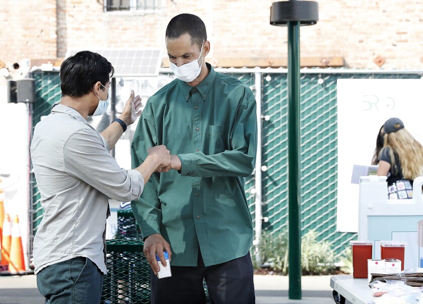 Two people in masks meeting with a fist-bump on skid row
