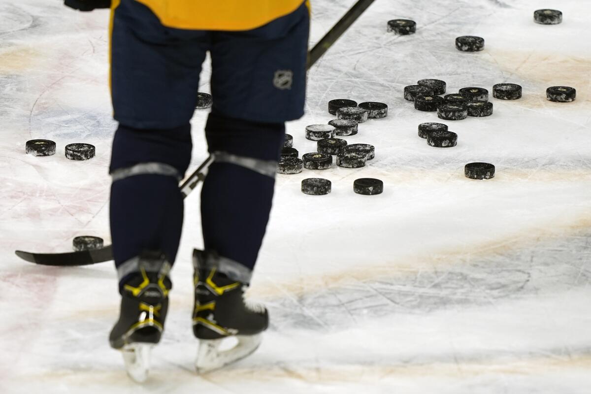 A Nashville Predators player shown from behind from the legs down skates past pucks.