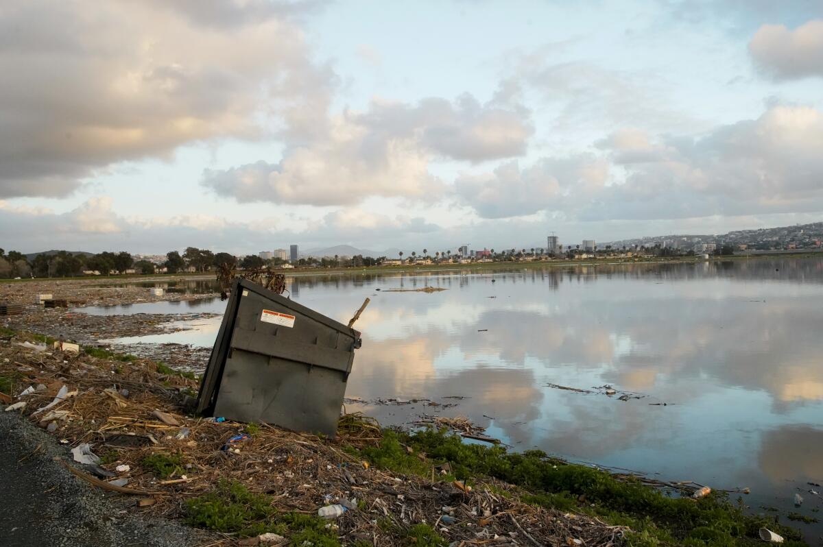 A flooded field with massive buildup of trash, raw sewage, and debris litters the Tijuana River Valley.