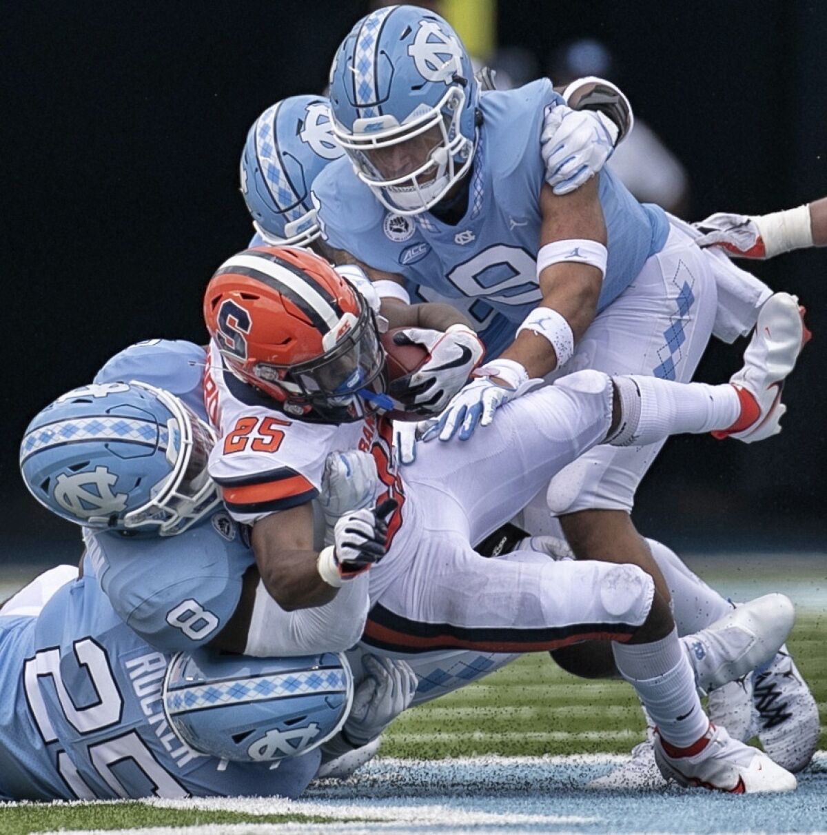Syracuse running back Jawhar Jordan (25) is stopped by North Carolina's Kaimon Rucker (25), Khadry Jackson (8), and Cam'Ron Kelly (9) in the fourth quarter of an NCAA college football game Saturday, Sept. 12, 2020 in Chapel Hill, N.C. (Robert Willett/The News & Observer via AP, Pool)